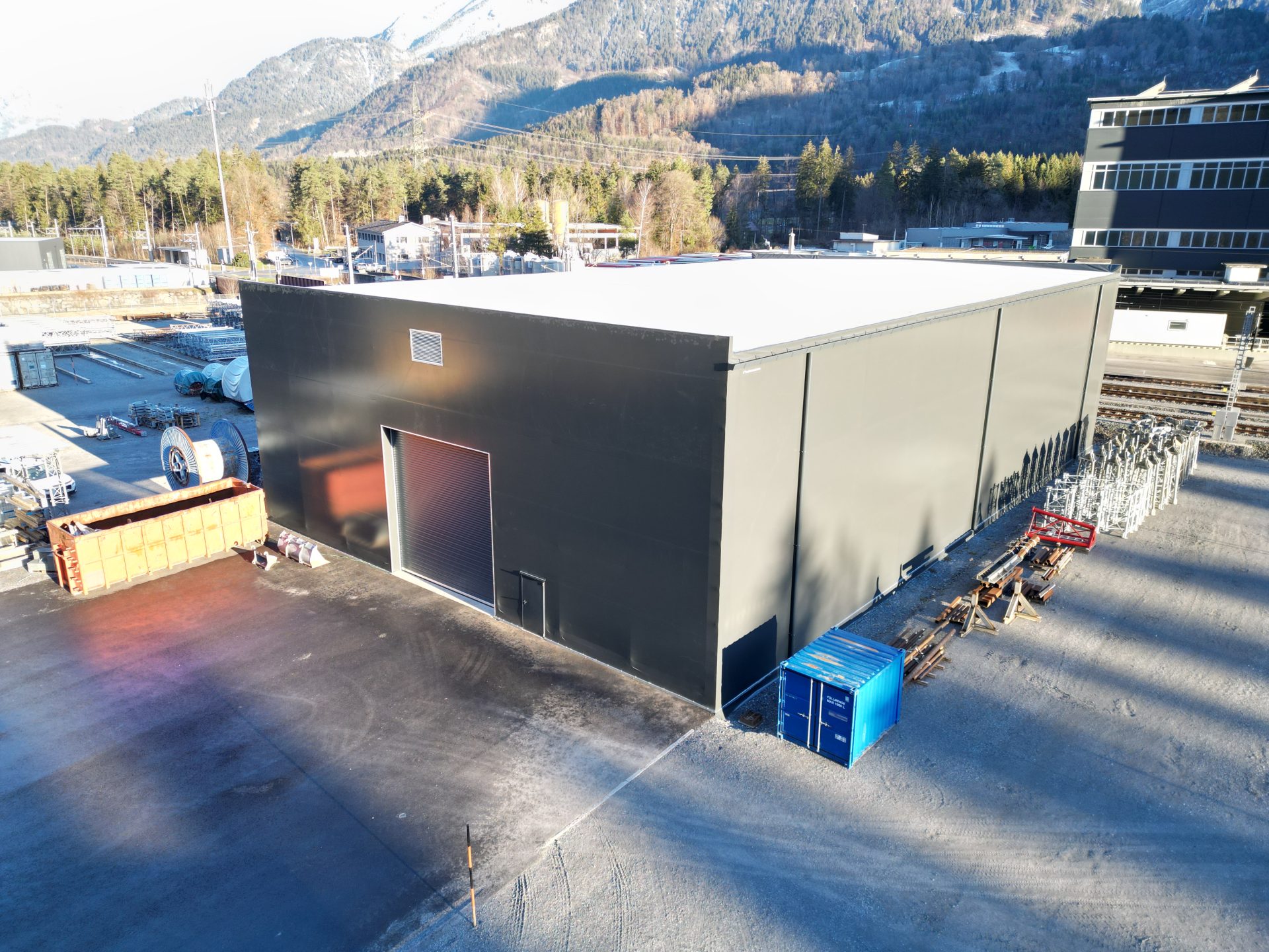 Grosses Zelt mit flachem Dach und Rolltor, umgeben von industriellen Elementen.