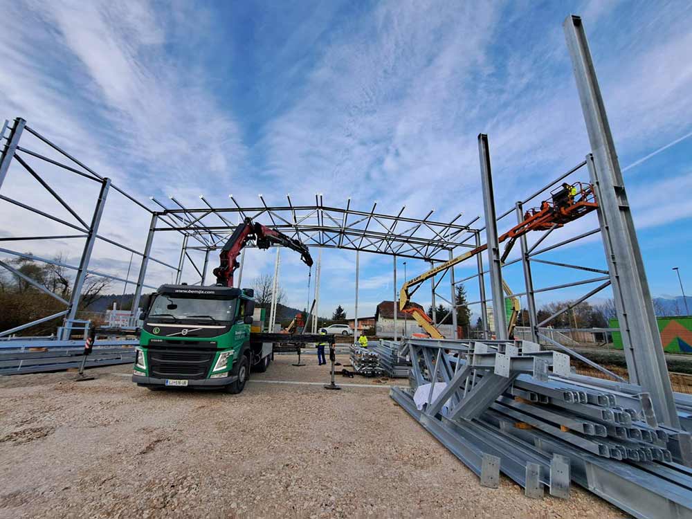 Montage der Stahlhalle mit Kran, LKW und Hebebühnen auf der Baustelle
